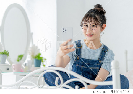 ベッドの上であぐらをかいてスマホを操作する女子高生 ベッドの上であぐらをかいてスマホを操作する女子高生 93616118