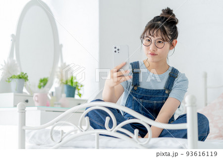 ベッドの上であぐらをかいてスマホを操作する女子高生 ベッドの上であぐらをかいてスマホを操作する女子高生 93616119