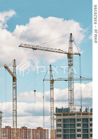 Industrial building cranes on background of cloudy sky. Hoisting cranes and multi-storey buildings of new city districts. Construction site background. Industrial building cranes on background of cloudy sky. Hoisting cranes and multi-storey buildings of new city districts. Construction site background. 93626566
