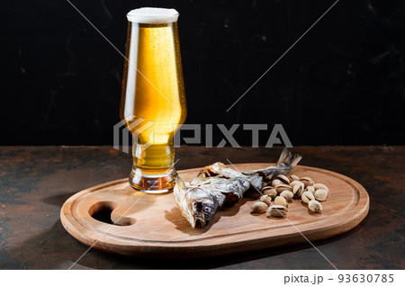 Amber beer in a narrow ale glass. Beer snack and foamy beer. Dried fish and pistachios. 93630785