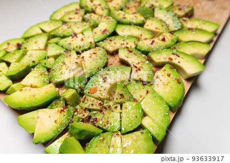 Avocado slices on a wooden textured background sprinkled with spices, bright accent. View from above Avocado slices on a wooden textured background sprinkled with spices, bright accent. View from above 93633917