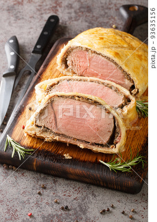 High angle beef wellington cooking or boeuf en crout cut into slices on a chopping board. Vertical 93635156