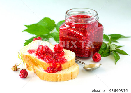 Homemade jam and white bread. Glass jar with raspberry jam on a white background. Preserved berry. 93640356