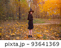 woman in witch costume with broom walking on covered with falling autumn leaves Halloween day forest 93641369