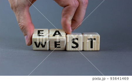 Hand turns a cube and changes the word 'east' to 'west', or vice versa. Beautiful grey background, copy space. Business concept. 93641469