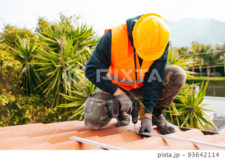 Technical worker works with drill on the roof of a house 93642114