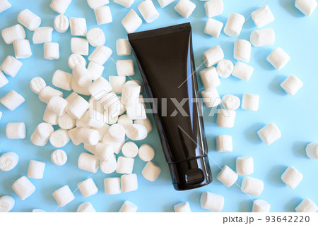 Mockup black squeeze bottle cosmetic tube and white mini marshmallows a lot on blue background. Cream, lubricant gel, moisturizer, skin care, sunscreen. Flat lay, top front view, blank tube 93642220