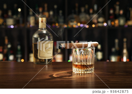 close up view of cigar, bottle of whiskey and a glass aside on color back. close up view of cigar, bottle of whiskey and a glass aside on color back. 93642875