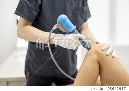 Doctor applies shock wave therapy on women's knee 93642957