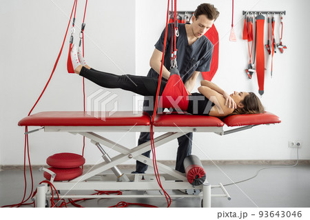 Rehabilitation specialist doing active treatment on suspension straps to a male patient Rehabilitation specialist doing active treatment on suspension straps to a male patient 93643046