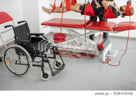 Rehabilitation specialist doing active treatment on suspension straps to a male patient Rehabilitation specialist doing active treatment on suspension straps to a male patient 93643048