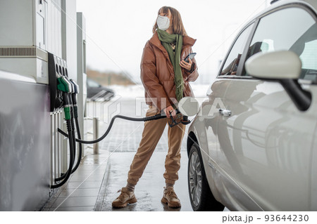 Woman in face mask refueling car with a gasoline using smart phone 93644230