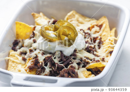 nachos with beef minced meat and cheese served with whipped cream and jalapenos nachos with beef minced meat and cheese served with whipped cream and jalapenos 93644359