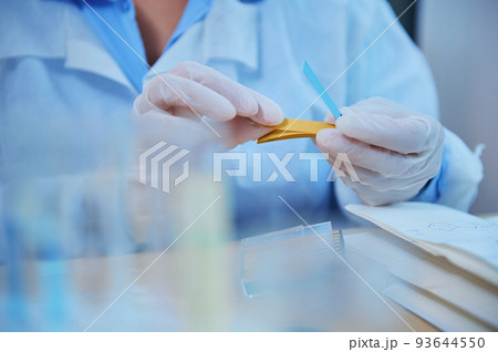Details: Hands in protective medical gloves of scientist, lab assistant holding a PH indicator strip for measuring the alkalinity and acidity of chemical substances in clinical research laboratory Details: Hands in protective medical gloves of scientist, lab assistant holding a PH indicator strip for measuring the alkalinity and acidity of chemical substances in clinical research laboratory 93644550