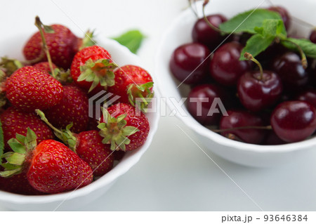 Two white plates with cherries and strawberries with mint petals stand on a white background, side view, close-up. High quality photo 93646384
