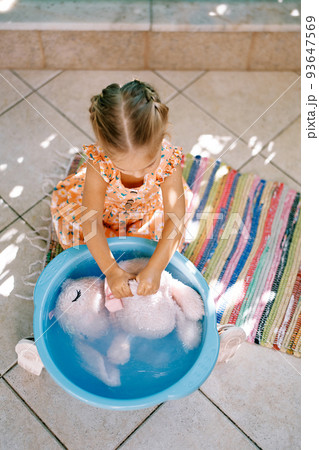 Little girl diligently lathers and rubs a soft toy in a bowl. High quality photo 93647569