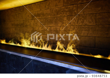 Side view on electric fireplace with artificial sparkling flame, decor for the interior, blue and orange flame with suspended swing chair in reflection. Side view on electric fireplace with artificial sparkling flame, decor for the interior, blue and orange flame with suspended swing chair in reflection. 93648753