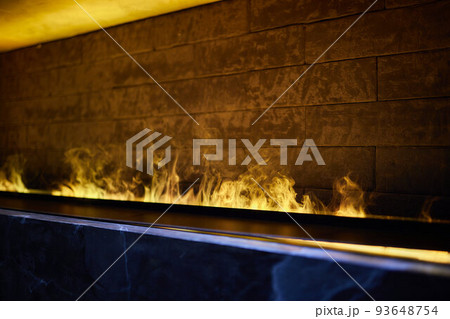 Side view on electric fireplace with artificial sparkling flame, decor for the interior, blue and orange flame with suspended swing chair in reflection. 93648754