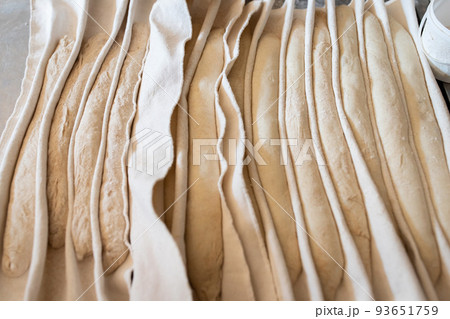The process of making traditional French baguettes in a craft bakery. Proofing bread on fabric. Front view. The process of making traditional French baguettes in a craft bakery. Proofing bread on fabric. Front view. 93651759