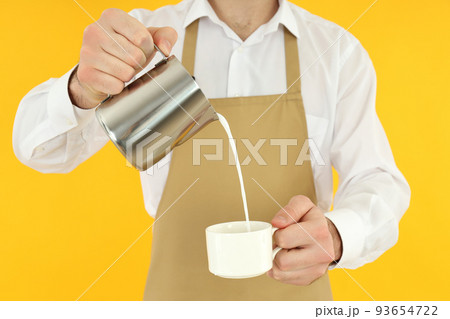 Waiter man pour milk on yellow background 93654722