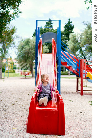 Little girl laughs while sitting down on a slide in the playground. High quality photo 93656859