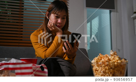 Young woman in warm sweater using mobile phone on couch, spending time in cozy winter or autumn weekend at night Young woman in warm sweater using mobile phone on couch, spending time in cozy winter or autumn weekend at night 93656957