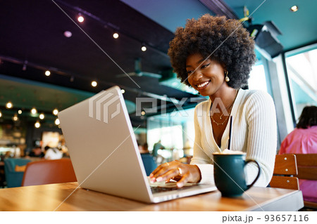 Smiling young african woman sitting with laptop in cafe 93657116