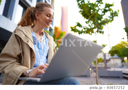 Young beautiful woman working on a laptop sitting on the bench in the street 93657252