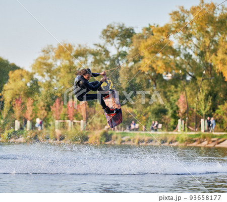 Wakeboarder making tricks while wakeboarding on lake. Young man surfer having fun wakesurfing in the cable park. Water sport, outdoor activity concept. 93658177