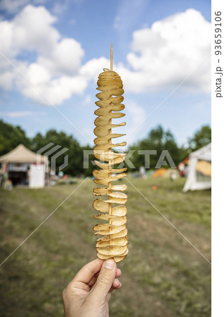 Potato street food snack in hand. Fried potatoes on a skewer at the food market festival. 93659106