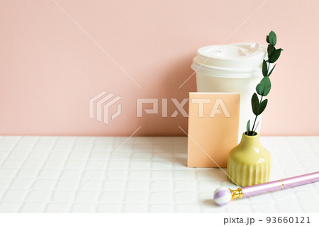 Paper coffee cup, memo pad, pen, dry plant on white desk. pink wall background 93660121
