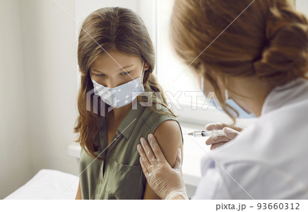 Preteen girl receives injection of antiviral vaccine against coronavirus in hospital. 93660312