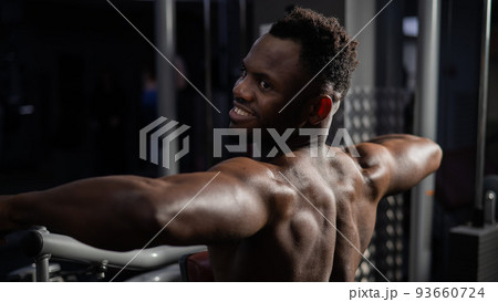 Shirtless african american man doing back exercises on a machine in the gym. Shirtless african american man doing back exercises on a machine in the gym. 93660724
