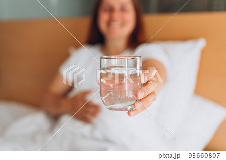 Pregnant woman with glass of water sitting on bed at home. Millennial Caucasian woman wake up in cozy white bed in modern apartment in the morning. Concept of healthy lifestyle, selective focus Pregnant woman with glass of water sitting on bed at home. Millennial Caucasian woman wake up in cozy white bed in modern apartment in the morning. Concept of healthy lifestyle, selective focus 93660807