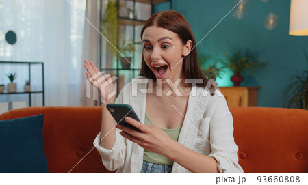 Happy lovely girl at home couch use smartphone typing browsing say wow yes found out great big win 93660808