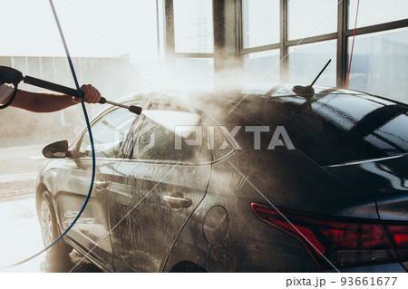 A man washes his car at a self-service car wash using a hose with pressurized water A man washes his car at a self-service car wash using a hose with pressurized water 93661677