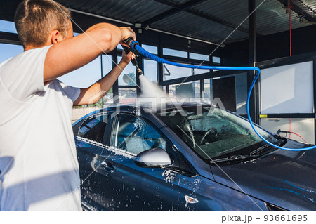 A man washes his car at a self-service car wash using a hose with pressurized water 93661695
