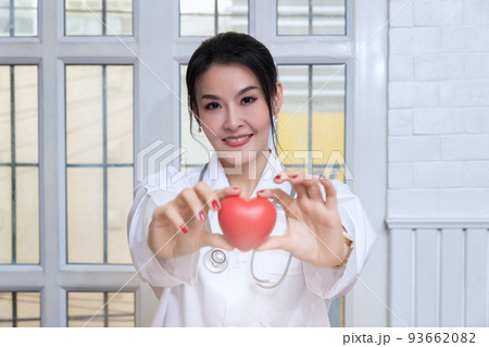 Female doctor holding a red heart ball in the hospital. Concept of health care and medical. Female doctor holding a red heart ball in the hospital. Concept of health care and medical. 93662082