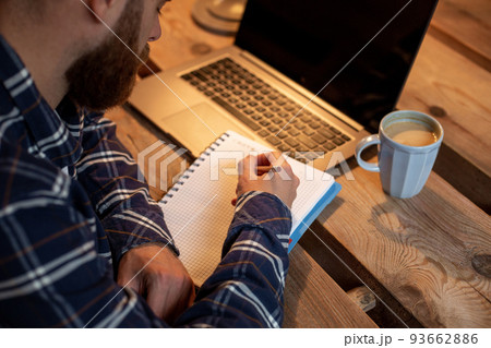 Cropped image of casual business man or freelancer planning his work on notebook, working on laptop computer with smart phone, cup of coffee on table at coffee shop or home office. 93662886
