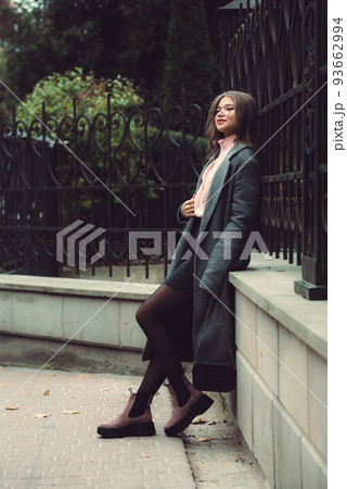 Fashionable and beautiful young woman 16-20 years old, dressed in an pink knitted sweater, glasses, dark skirt and a gray classic trench coat and ankle boots Fashionable and beautiful young woman 16-20 years old, dressed in an pink knitted sweater, glasses, dark skirt and a gray classic trench coat and ankle boots 93662994