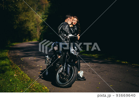 Handsome young man and beautiful young girl, couple sitting on a motorcycle, standing near a motorcycle in black leather clothes, hugging, in nature, on the street Handsome young man and beautiful young girl, couple sitting on a motorcycle, standing near a motorcycle in black leather clothes, hugging, in nature, on the street 93669640