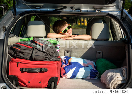 Adorable kid boy wearing sunglasses sitting in car trunk. Portrait of Happy child with open car boot while waiting for parent get ready for vocation. Family trip traveling by car concept Adorable kid boy wearing sunglasses sitting in car trunk. Portrait of Happy child with open car boot while waiting for parent get ready for vocation. Family trip traveling by car concept 93669886
