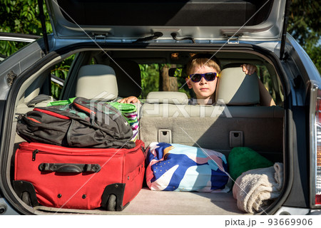 Adorable kid boy wearing sunglasses sitting in car trunk. Portrait of Happy child with open car boot while waiting for parent get ready for vocation. Family trip traveling by car concept 93669906