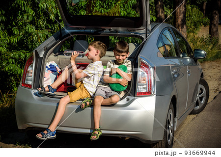 Two happy children boy and his brother sitting together in a car trunk. Cheerful kids hugging each other in family vehicle luggage compartment. Weekend travel and holidays concept 93669944