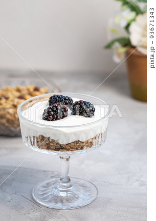 Dessert with yogurt, homemade granola and fresh blackberries, served in trendy patterned clear glass, gray background. Healthy vegan breakfast or snack. Copy space, selective focus 93671343