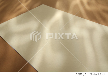empty white paper sheet on brown background with sunlight glow and shadows empty white paper sheet on brown background with sunlight glow and shadows 93671497
