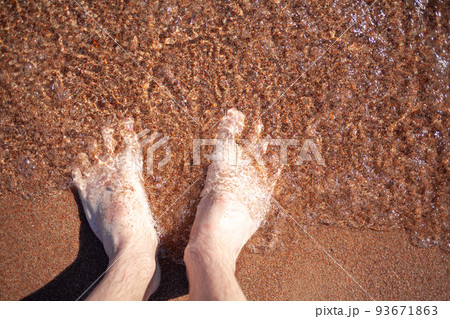 Top view of men's legs in the sea. A man is standing on the sand. 93671863
