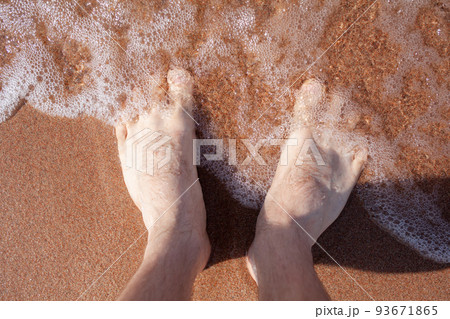 Top view of men's legs in the sea. A man is standing on the sand. 93671865
