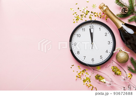New year celebration concept with a bottle of champagne and two glasses toasting. Christmas gift box, alarm clock and fir tree branch on colored table. Top view Copy space New year celebration concept with a bottle of champagne and two glasses toasting. Christmas gift box, alarm clock and fir tree branch on colored table. Top view Copy space 93672688