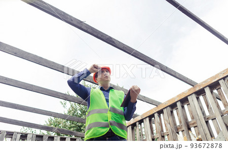 Building inspector. Man in a hard hat and a yellow reflective vest examines damaged structures and inspects the building. Damage assessment. Preparing for the repair or construction of a building Building inspector. Man in a hard hat and a yellow reflective vest examines damaged structures and inspects the building. Damage assessment. Preparing for the repair or construction of a building 93672878
